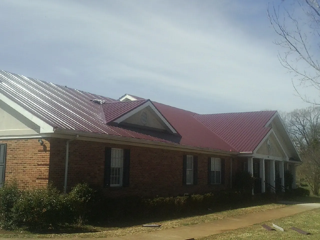 Red metal roof with gabled entries on a long brick building, from a Hail Damage Roof Repair job in Sergeant Bluff