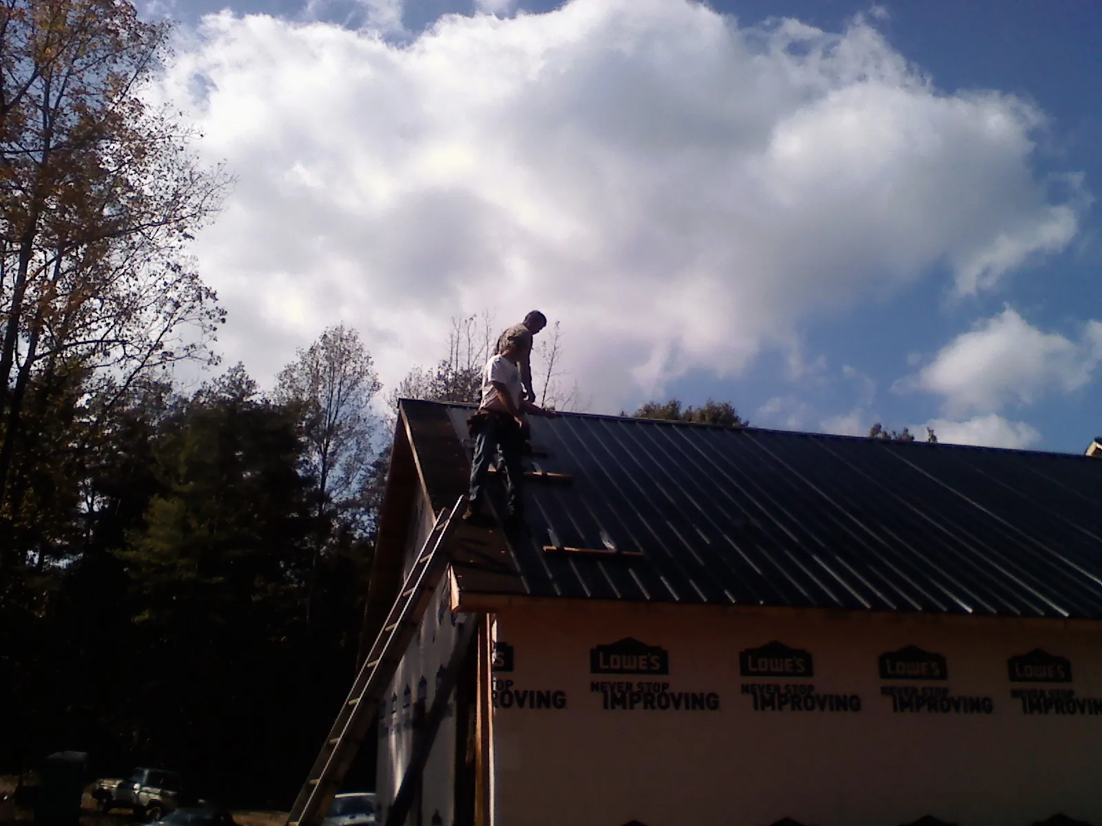 Roofer fastening dark metal panels high against a cloudy sky, from a Roof Inspection job in Sergeant Bluff