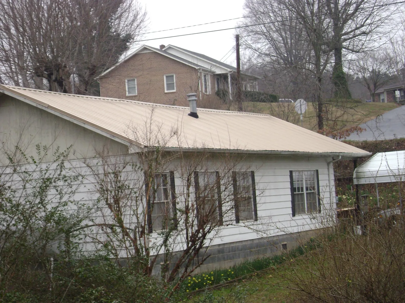 Tan metal roof on a white sided house set into a hillside — Commercial Roofing by Roofing Brothers in Sergeant Bluff